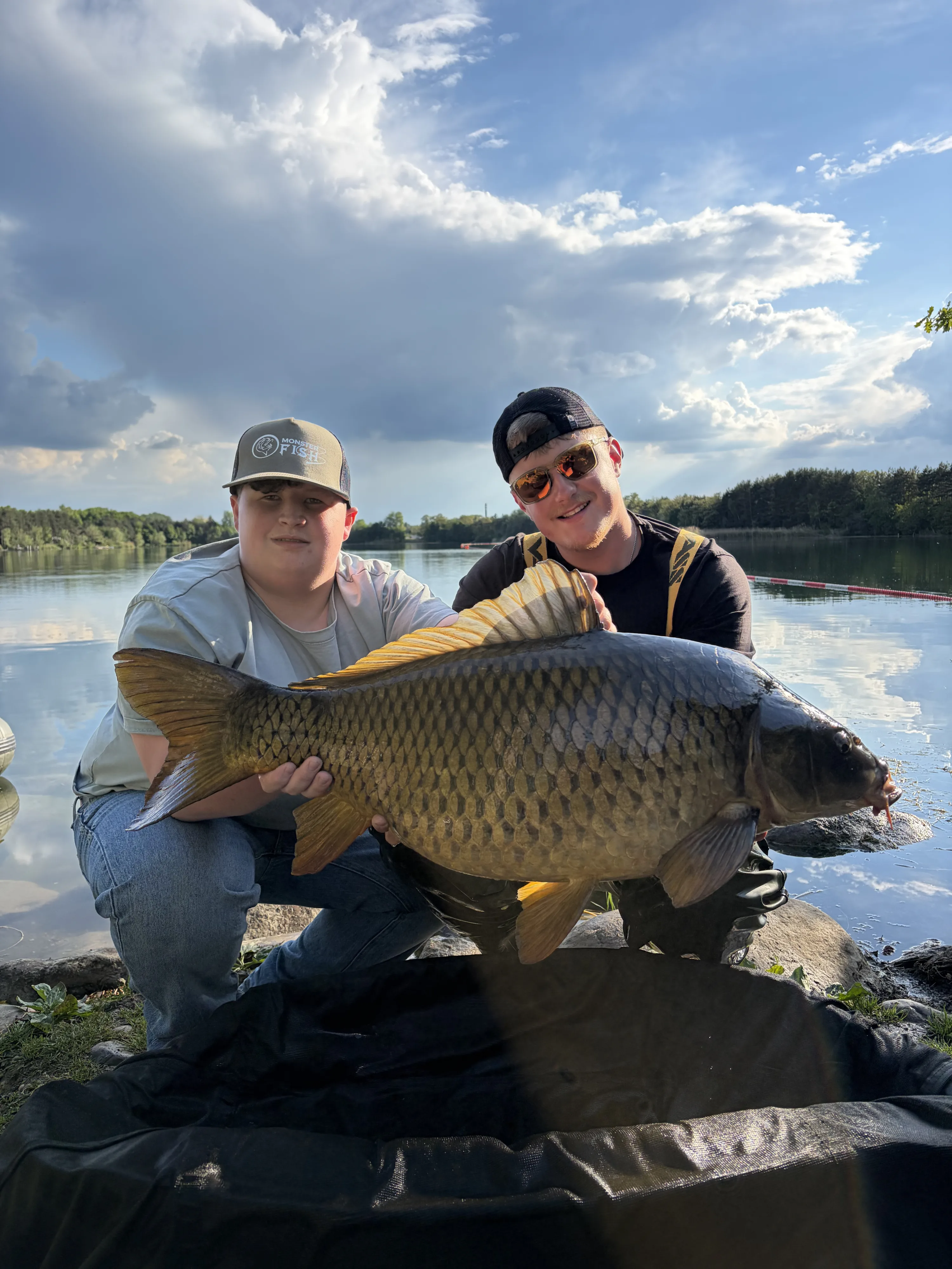 Zwei Angler präsentieren stolz einen großen Karpfen am See